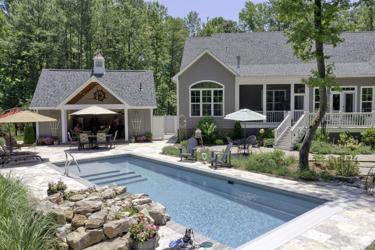 Backyard fiberglass pool with travertine deck and pool house