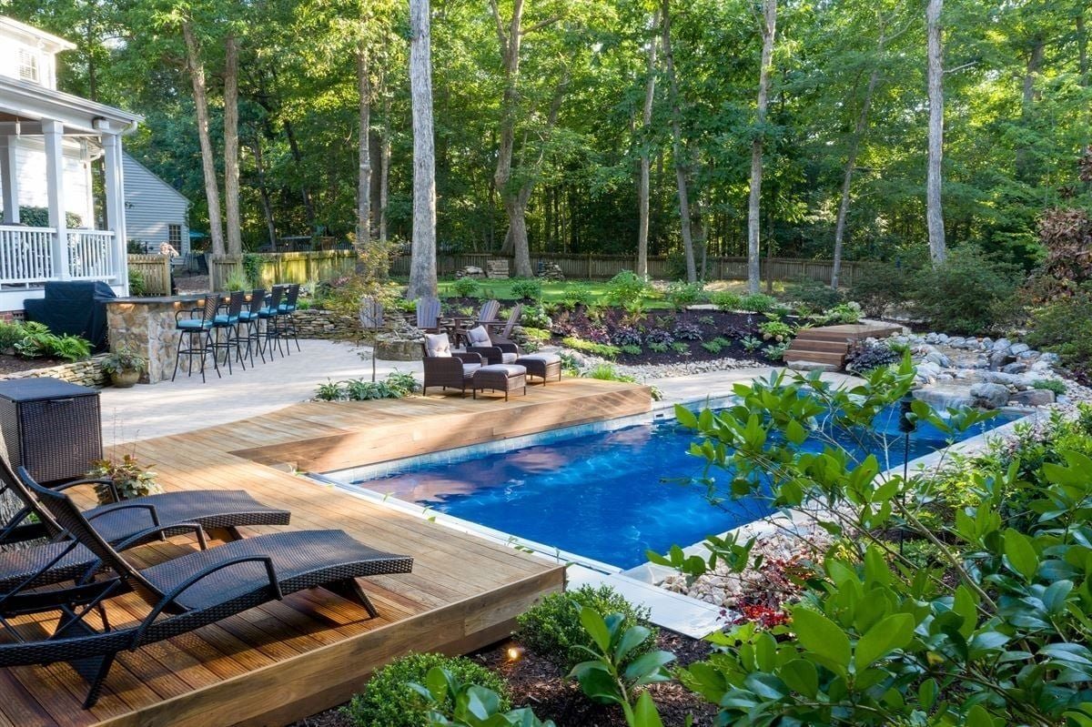 Fiberglass pool set into a wooded backyard with a wood deck